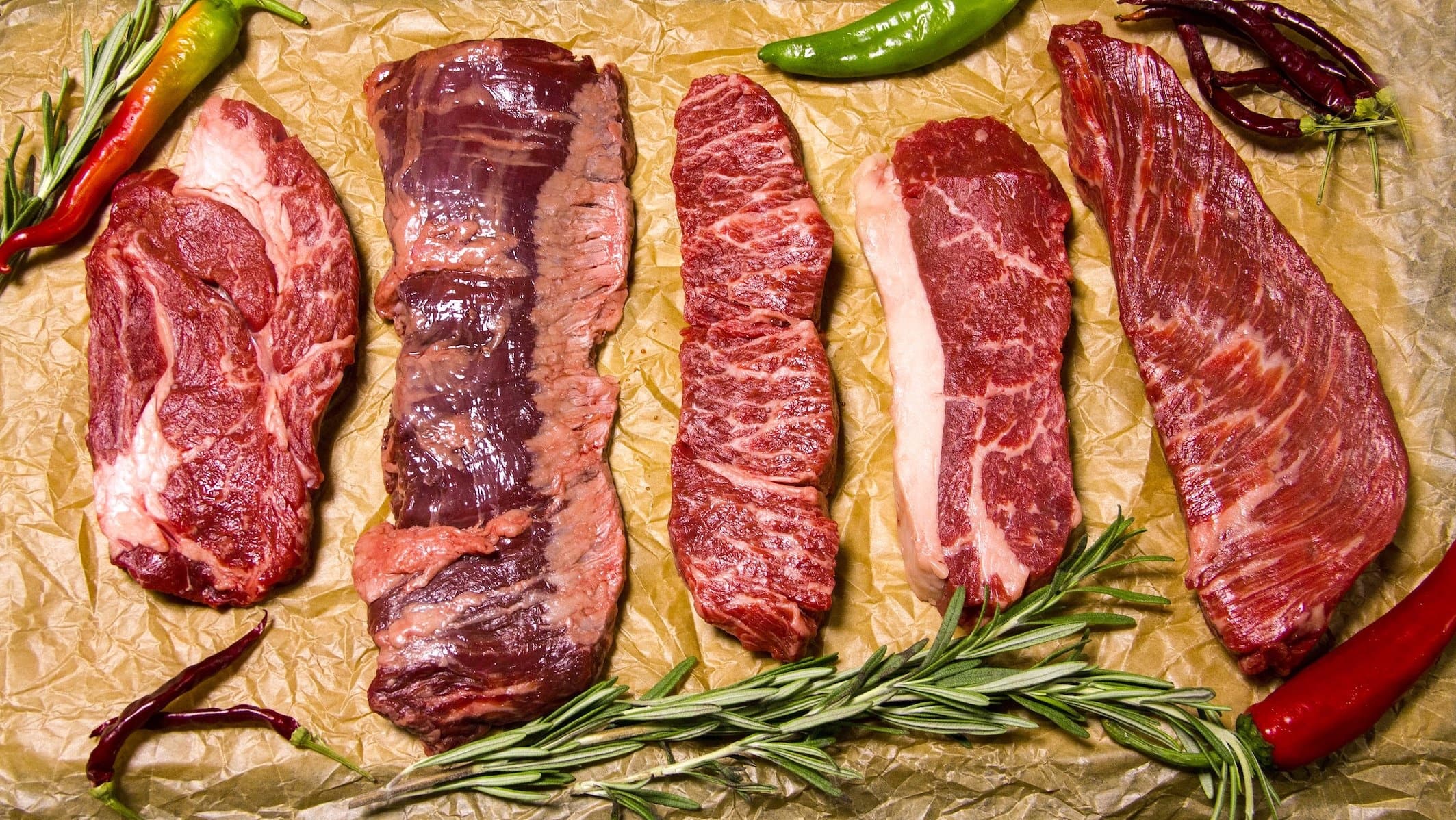 Assorted raw steaks on butcher paper with herbs for grilling