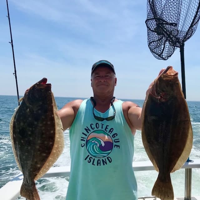Angler holding two flounder on deck with ocean background
