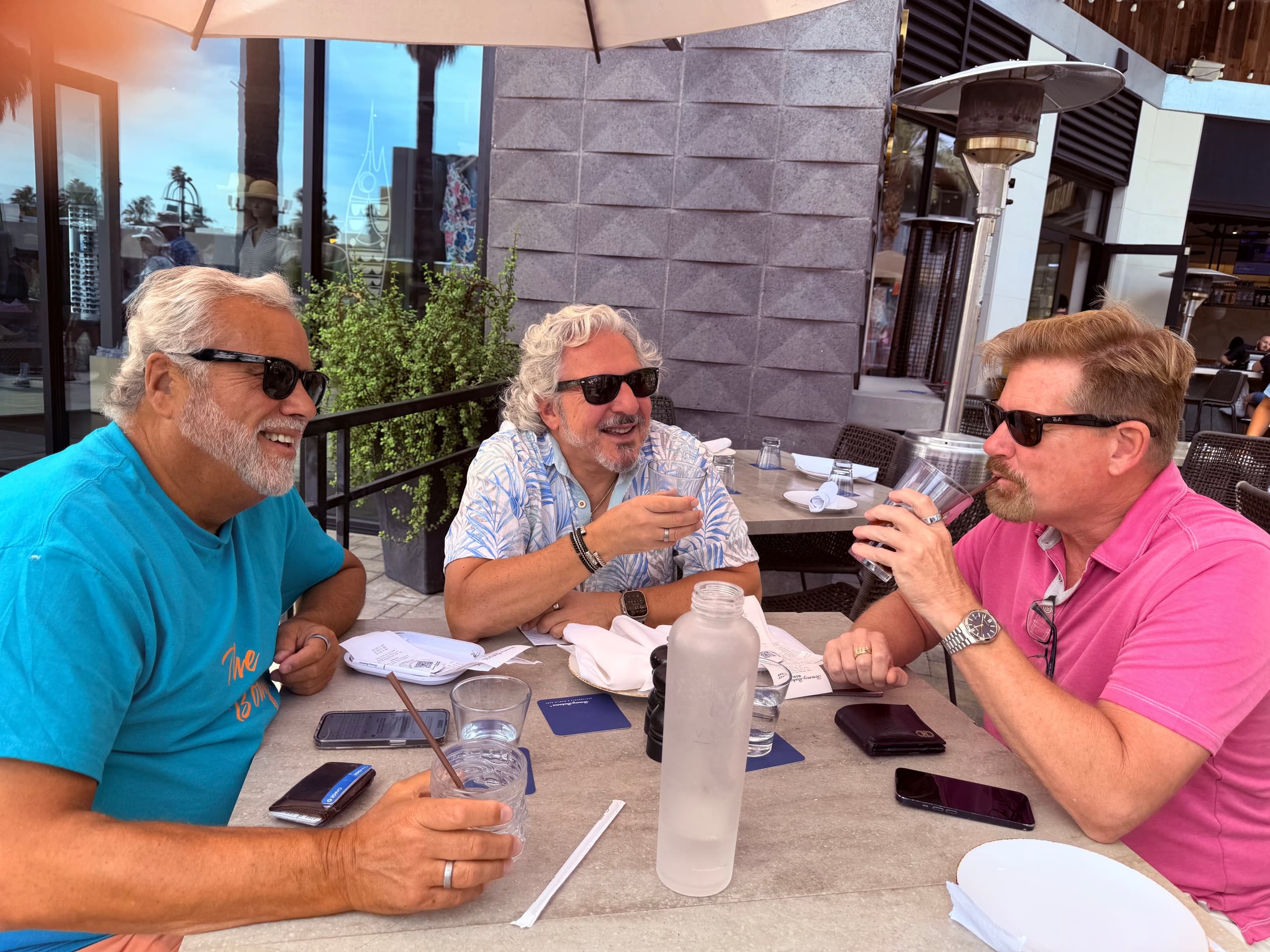 Friends laughing and sharing drinks at an outdoor sidewalk cafe