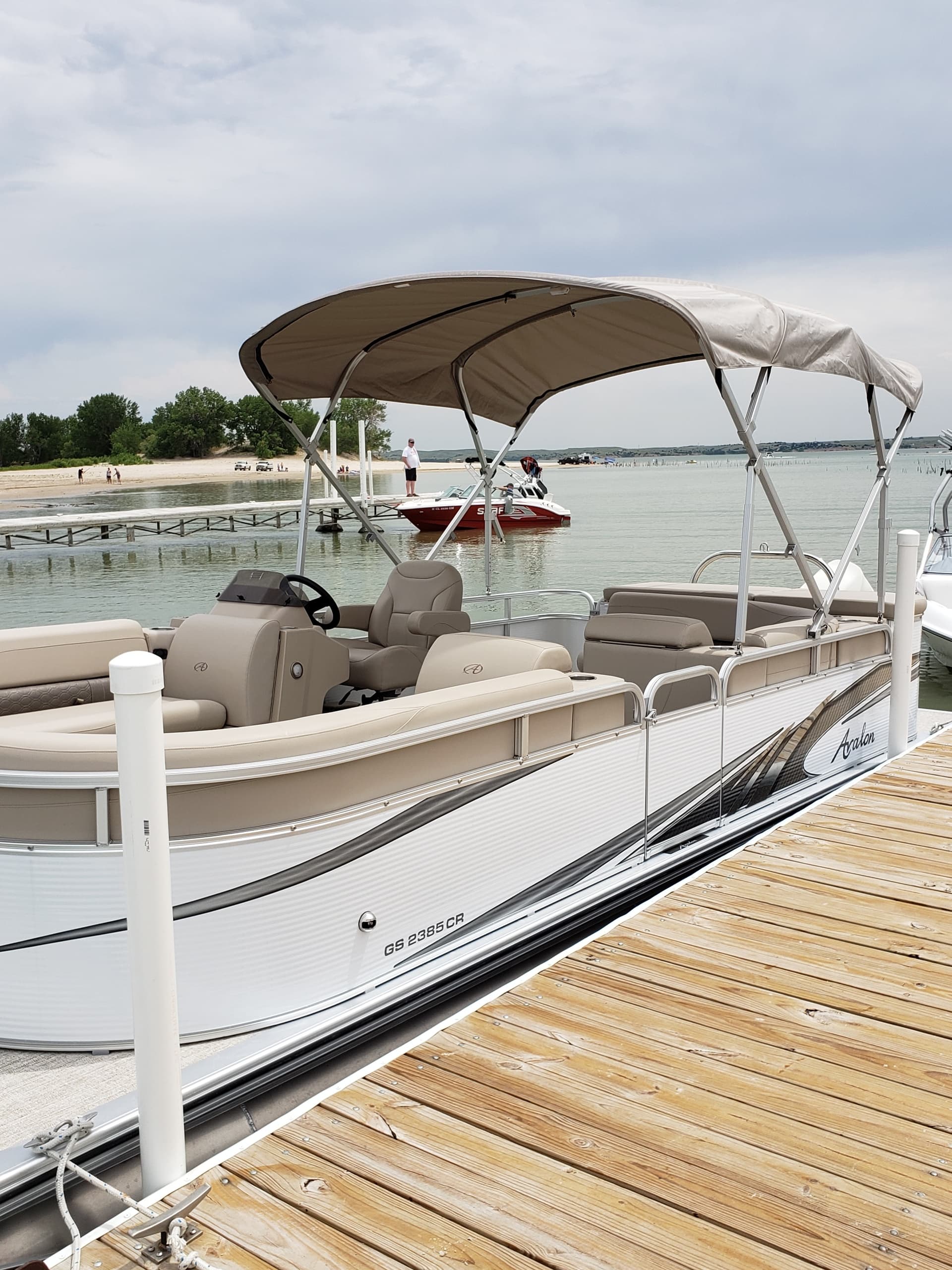 Pontoon boat moored at wooden dock with lake shoreline background