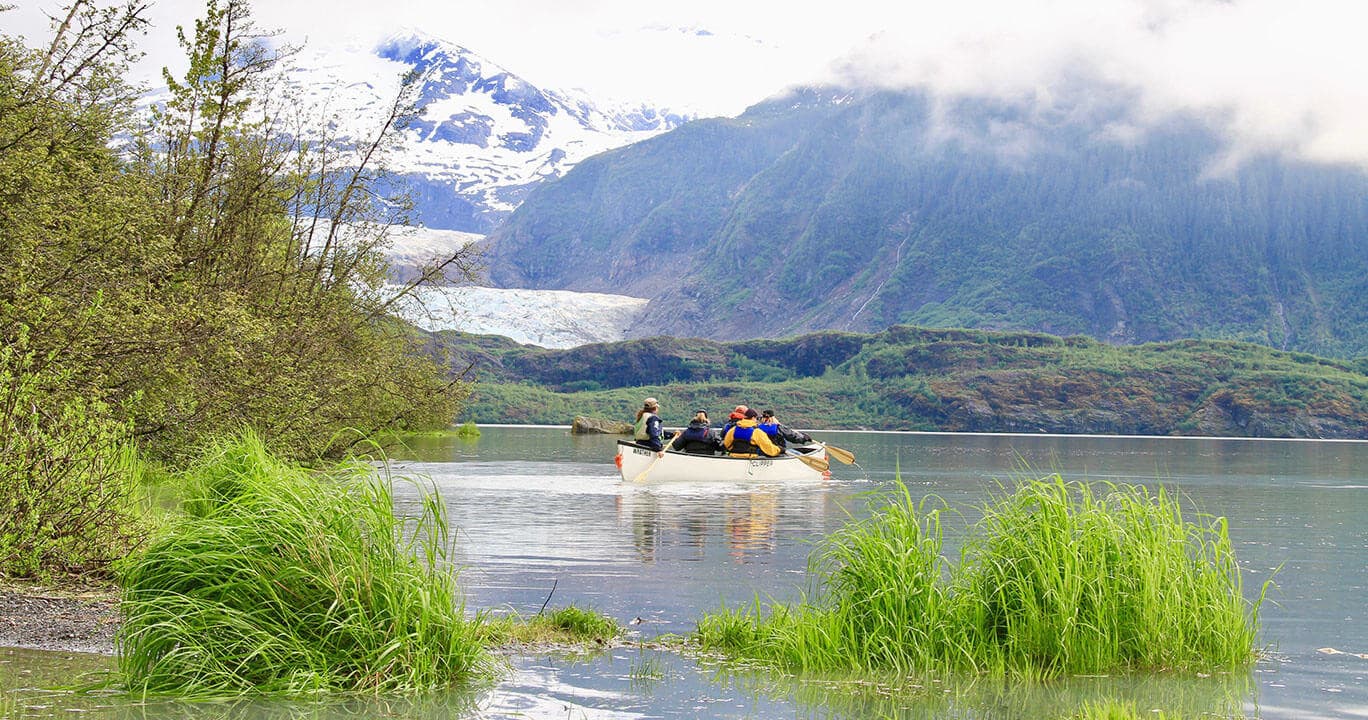 Canoeists rowing on calm mountain lake framed by glacier
