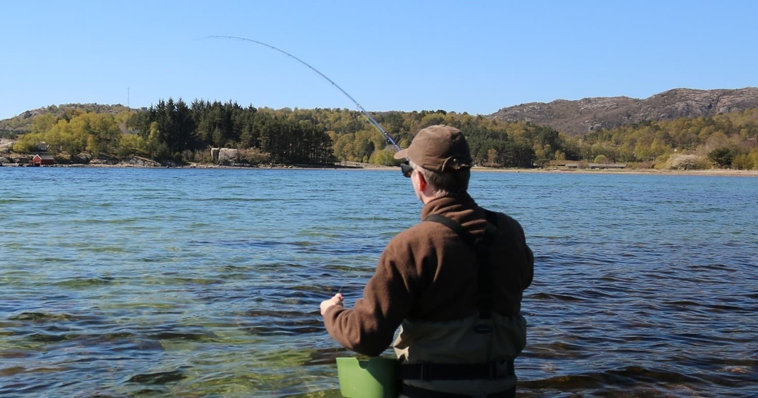 Angler casting on clear freshwater lake with forested hills