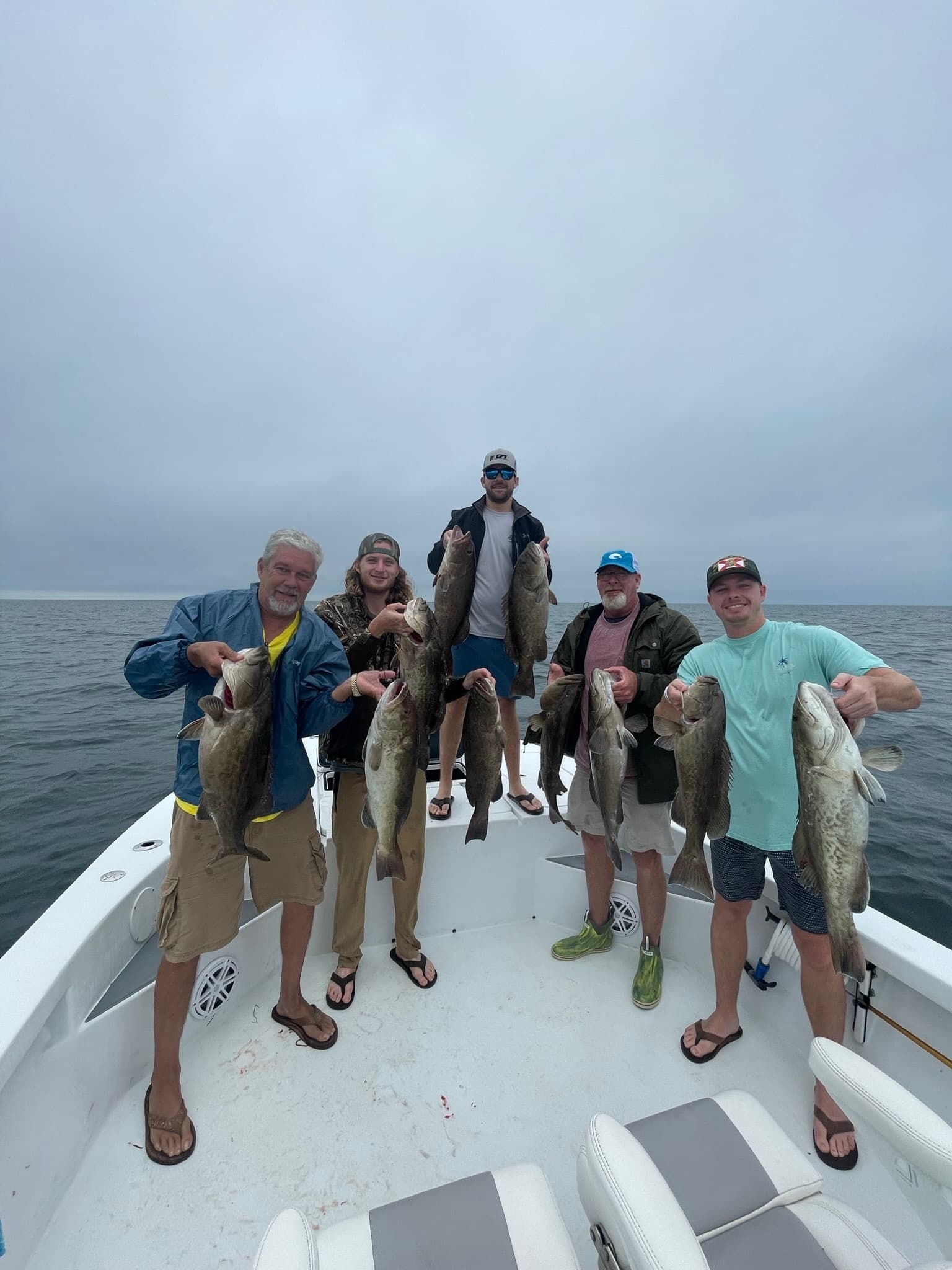 Charter anglers holding big coastal fish on overcast ocean deck