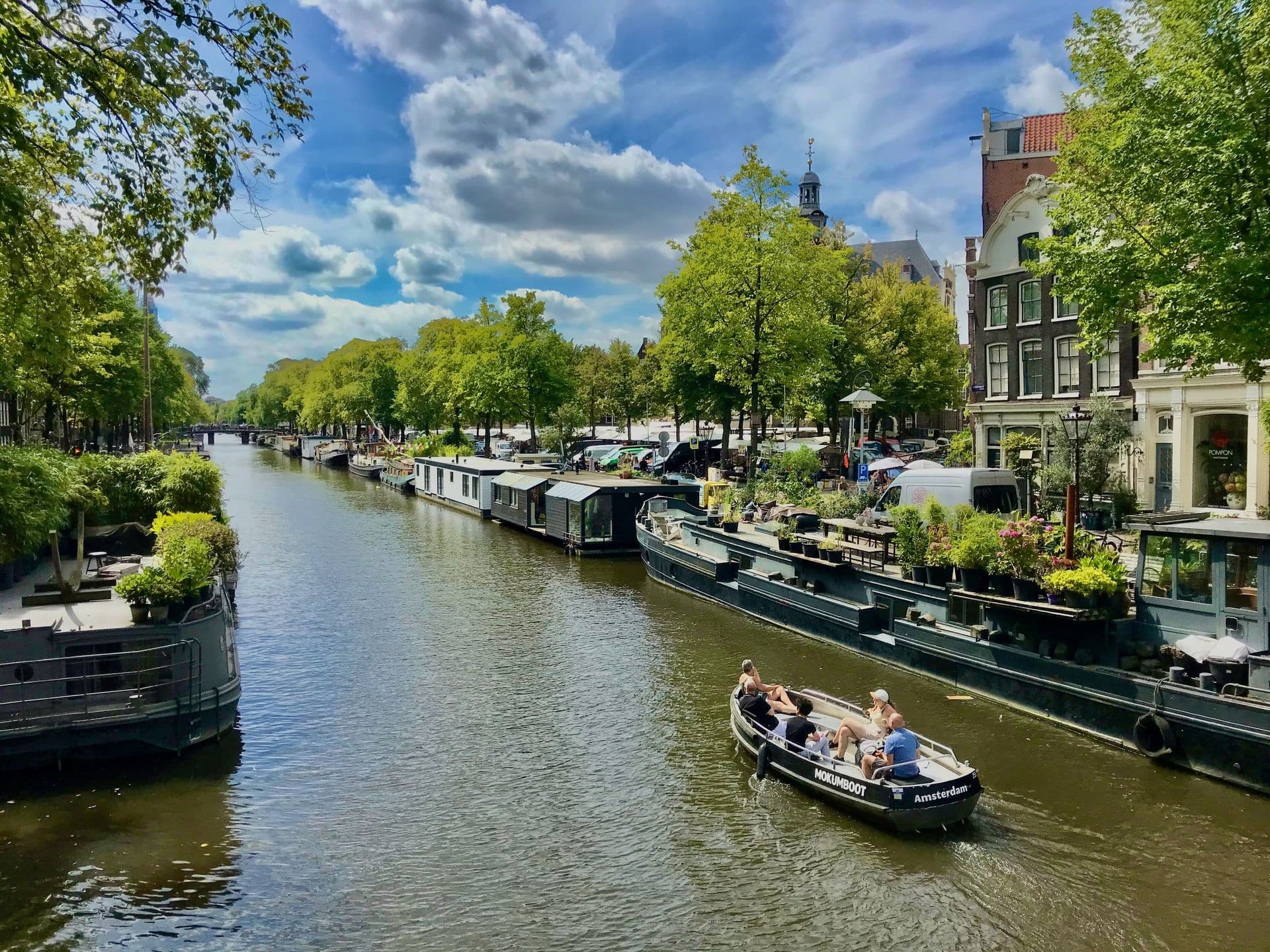 Canal boat cruising past tree-lined Amsterdam canal houses