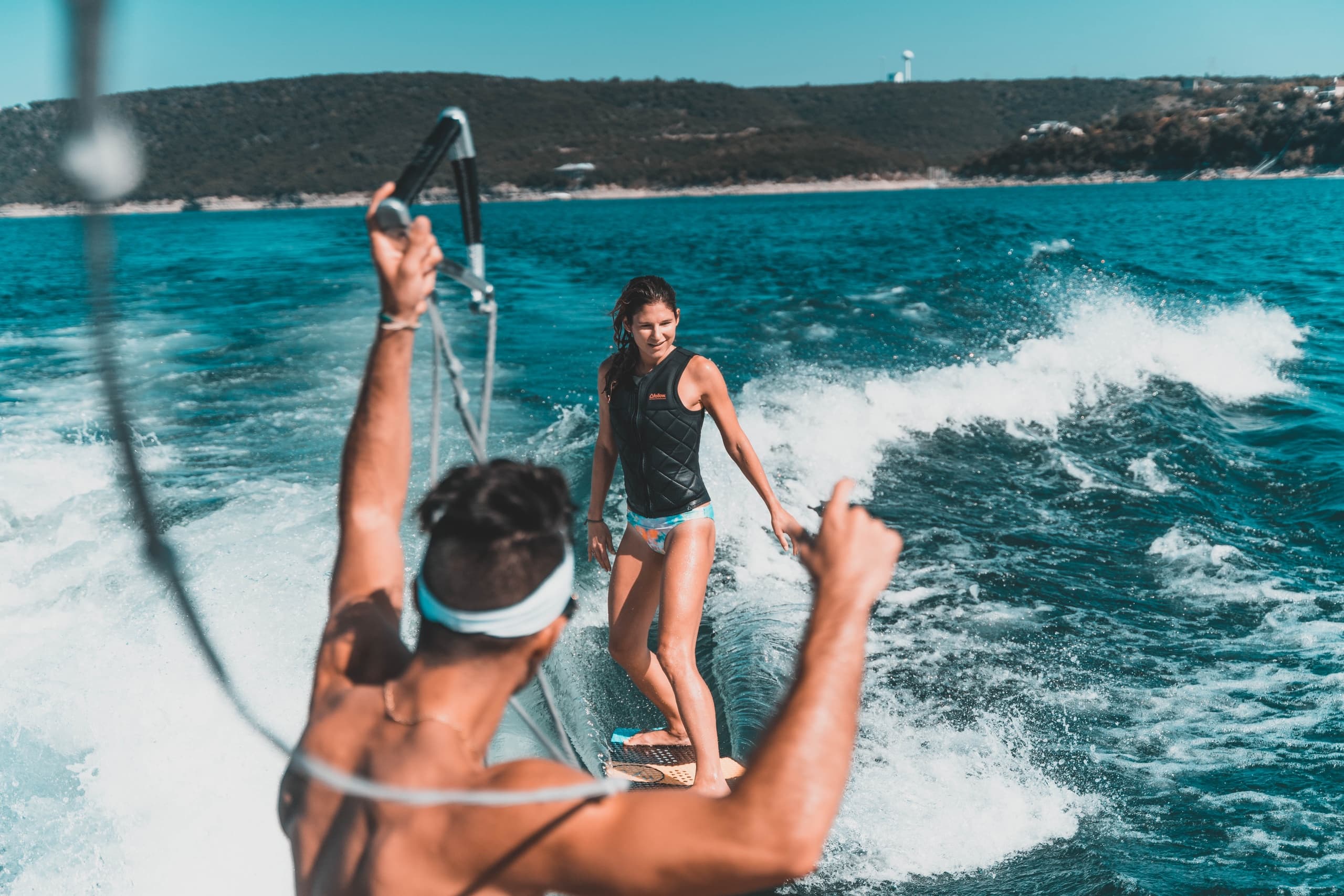 Couple wakesurfing behind boat on choppy blue open water