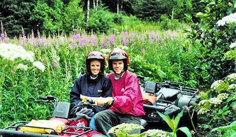Couple on ATVs smiling in wildflower meadow, Alaska tour