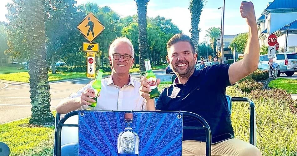 Two men enjoying pedicab ride with beers by palm trees