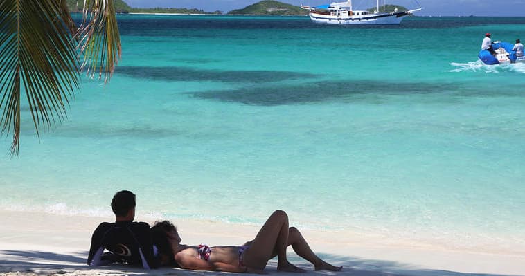Couple lounging on white tropical beach with turquoise sea