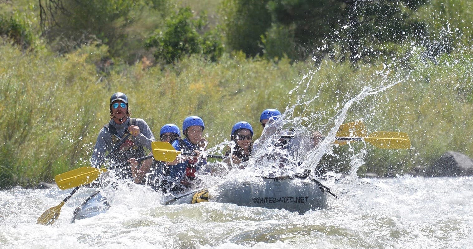 Rafting crew splashing through sunlit river rapid outdoors