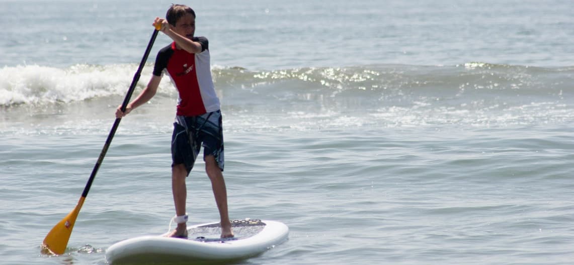 Stand-up paddleboarder paddling on calm ocean waves near shore