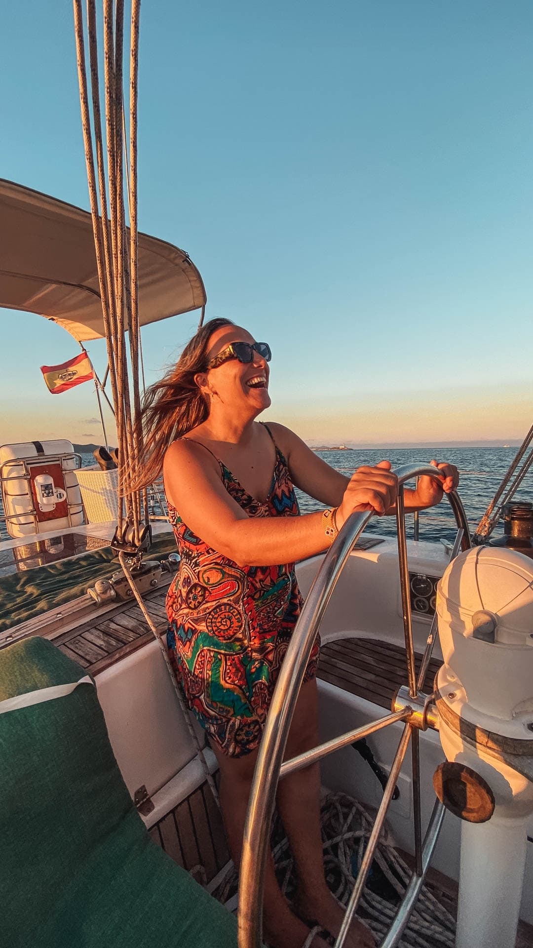 Woman steering a sailboat helm at sunset on open sea