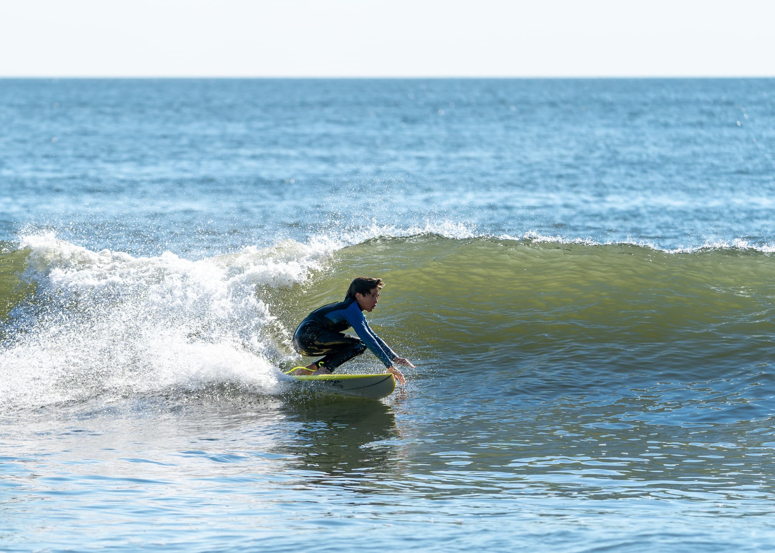 Surfer paddling toward rolling wave under expansive sky