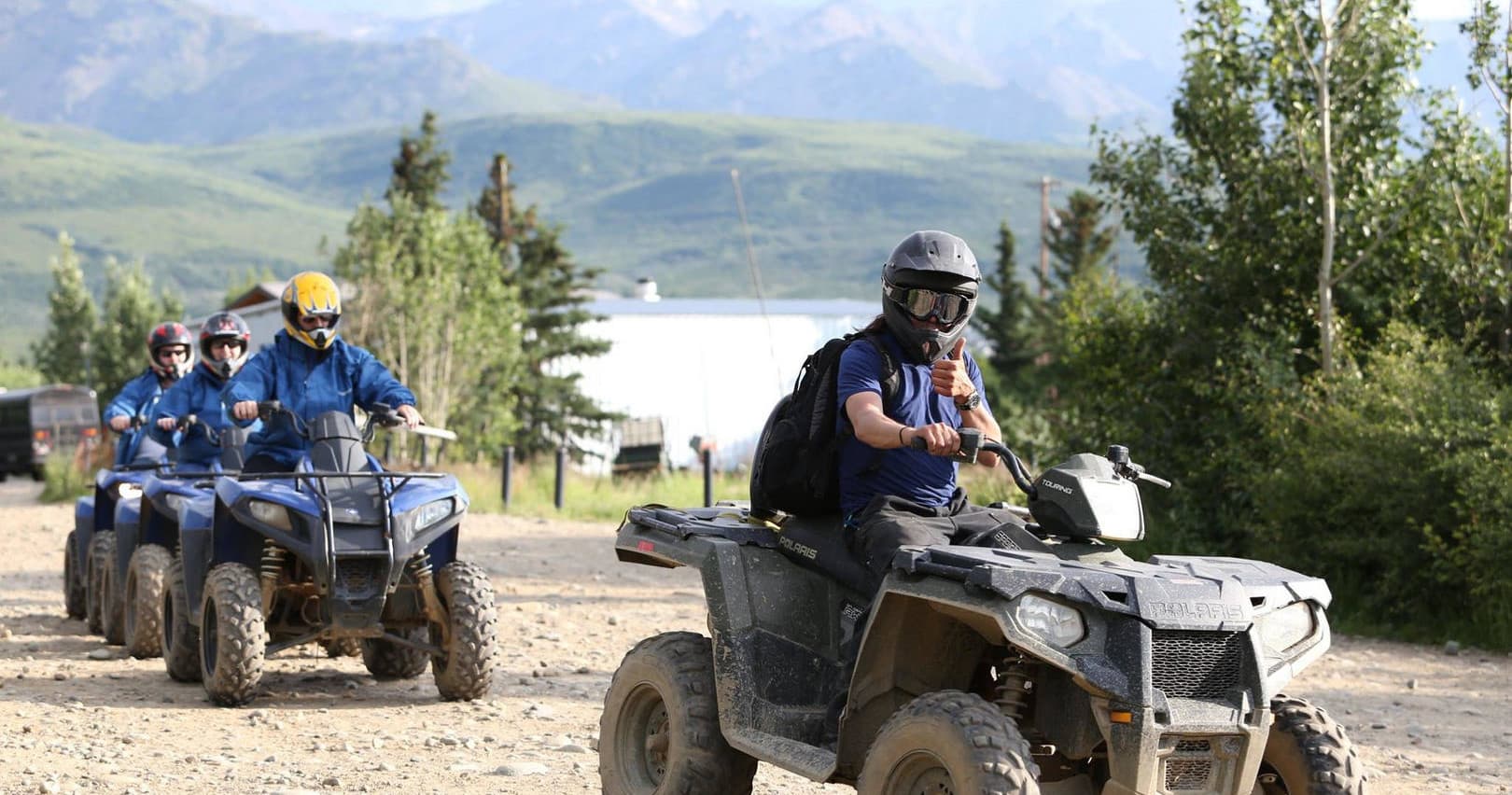 ATV riders traversing forested trail with mountain lake views
