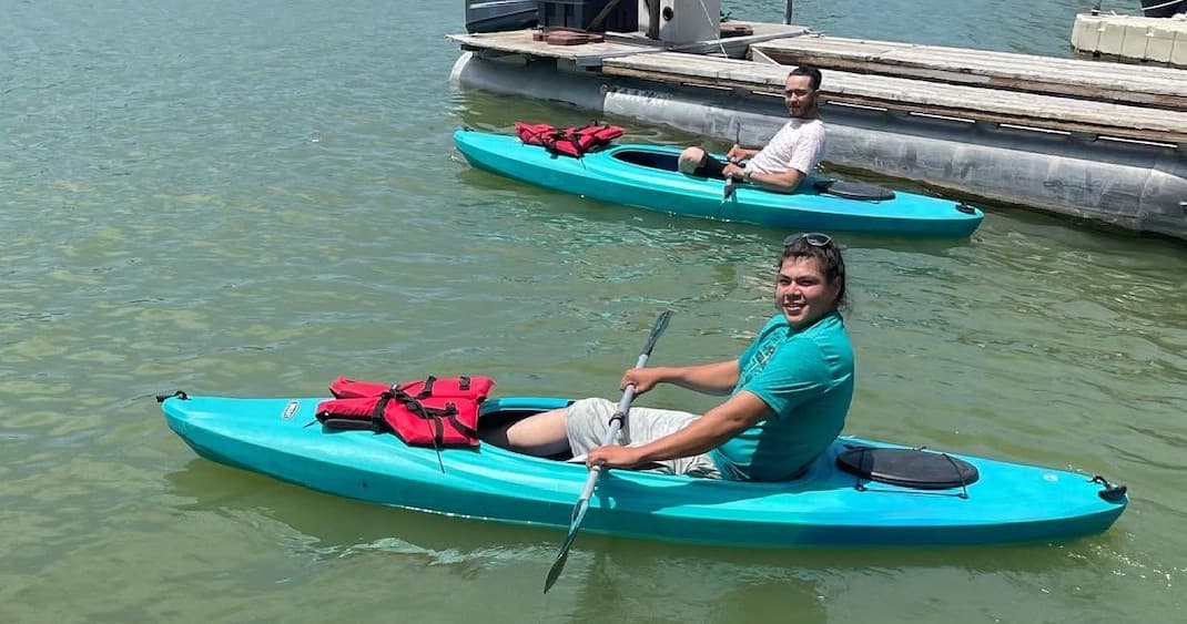 Solo kayaker paddling near marina on calm green lake water