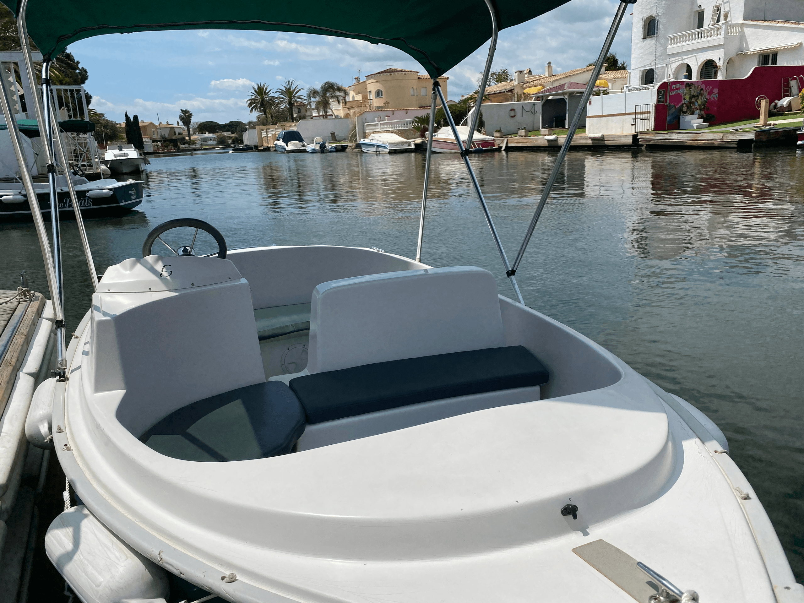Small electric boat cruising residential canal with bimini