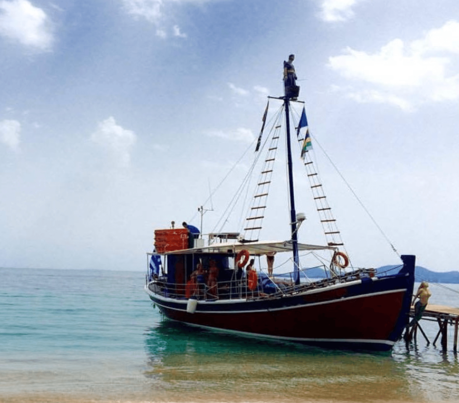 Traditional wooden boat docked at sandy shore with crew