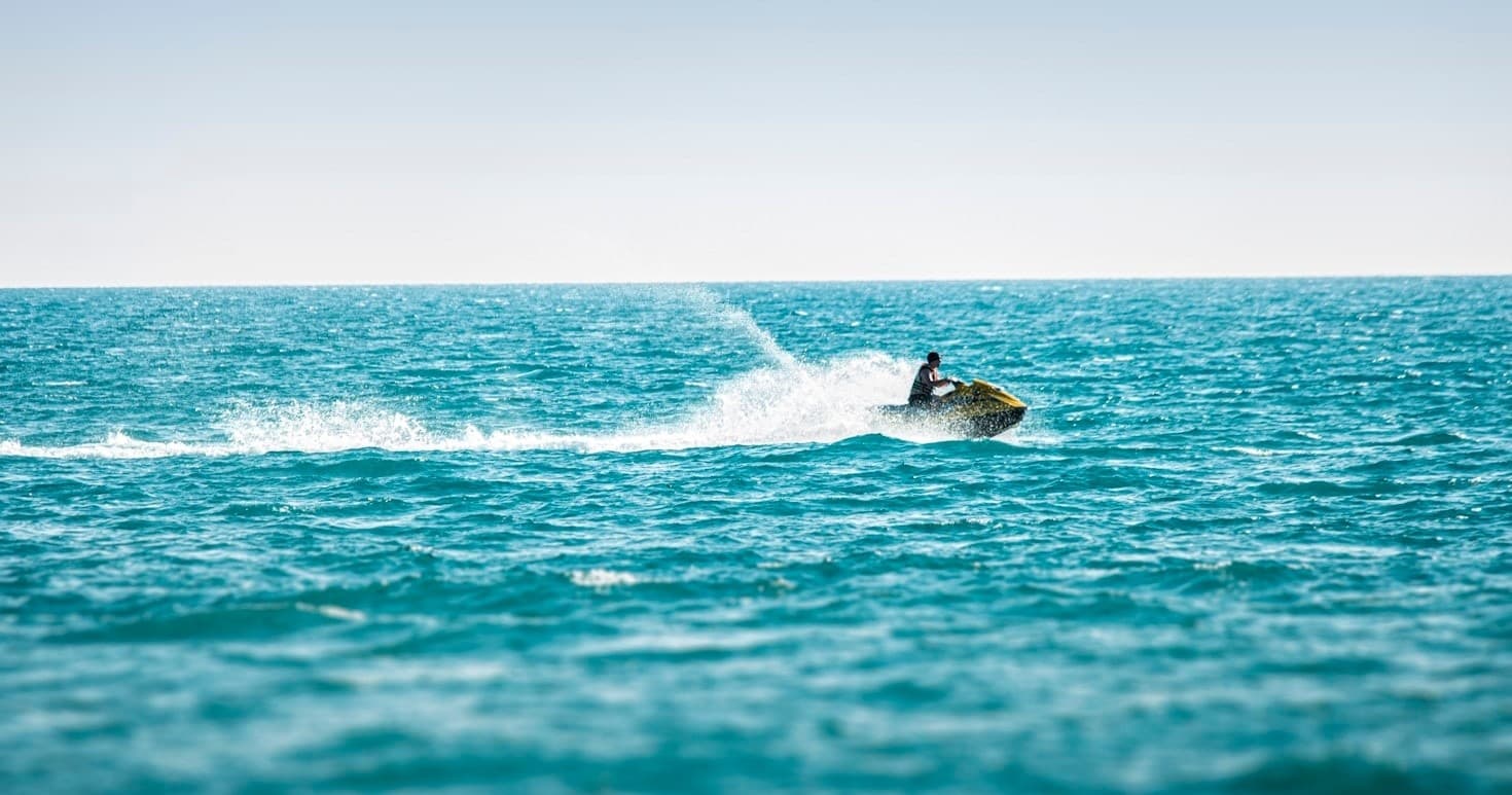 Jet ski rider speeding across turquoise ocean near coastline