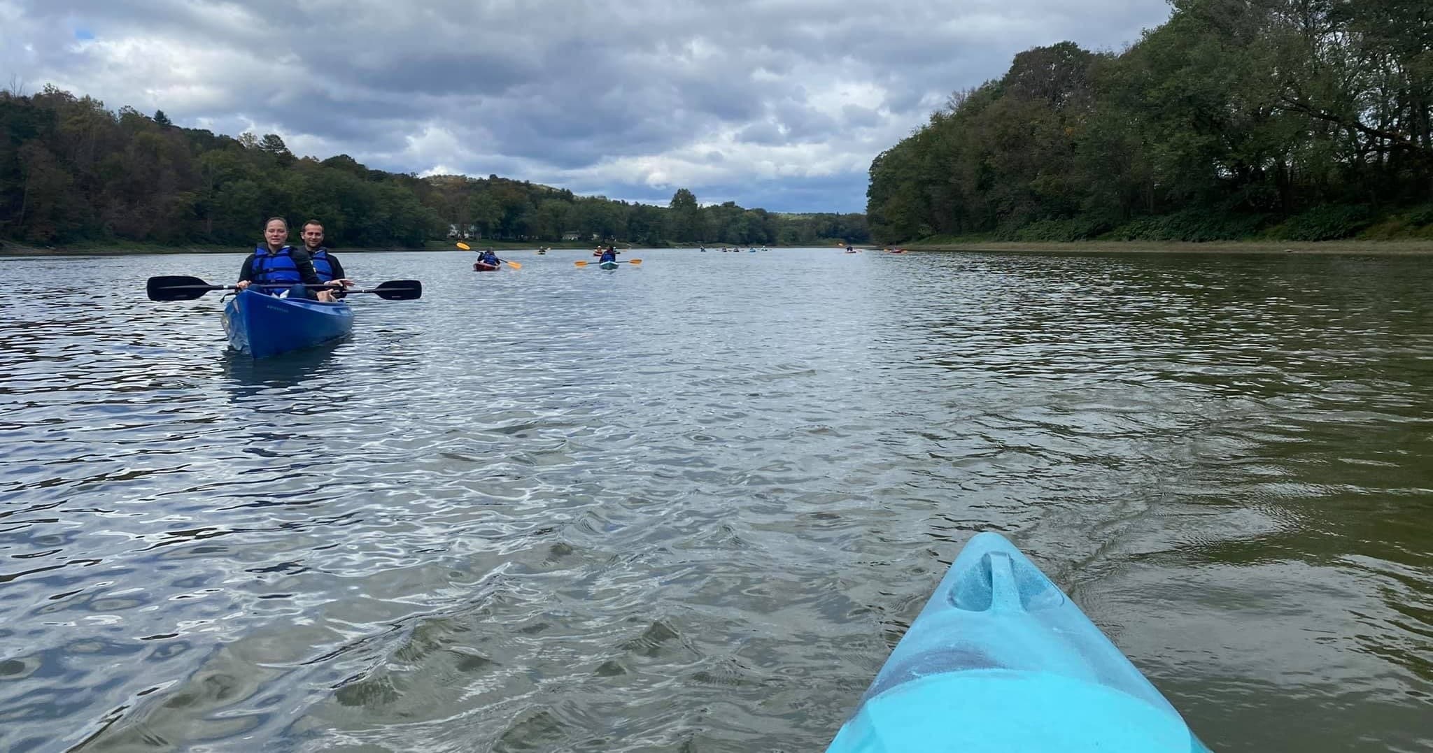 View from kayak bow paddling down tree-lined river