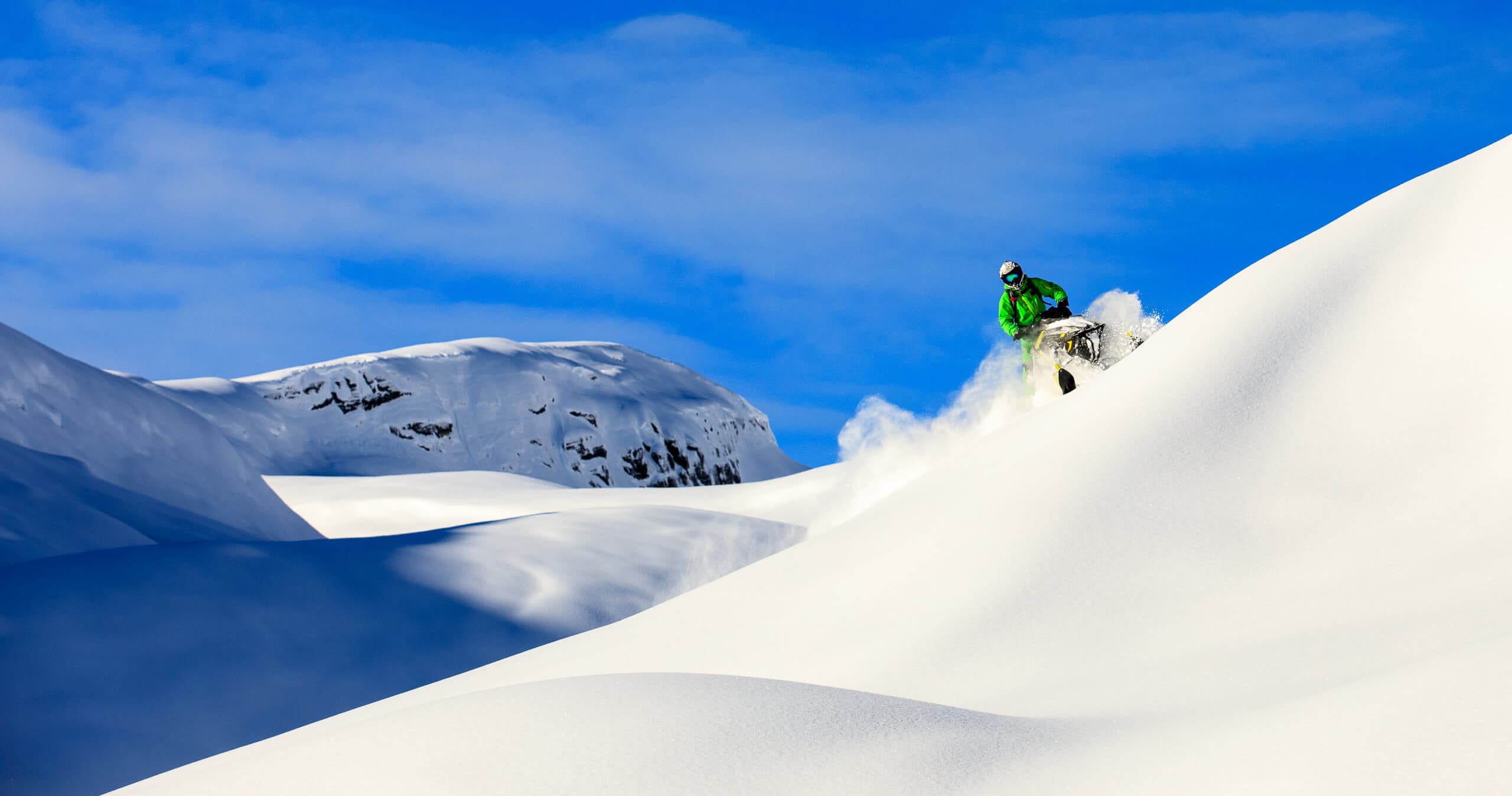 Snowmobiler riding over snowy alpine ridge with bright blue sky