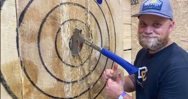 Man posing with axe embedded in wooden target at indoor venue