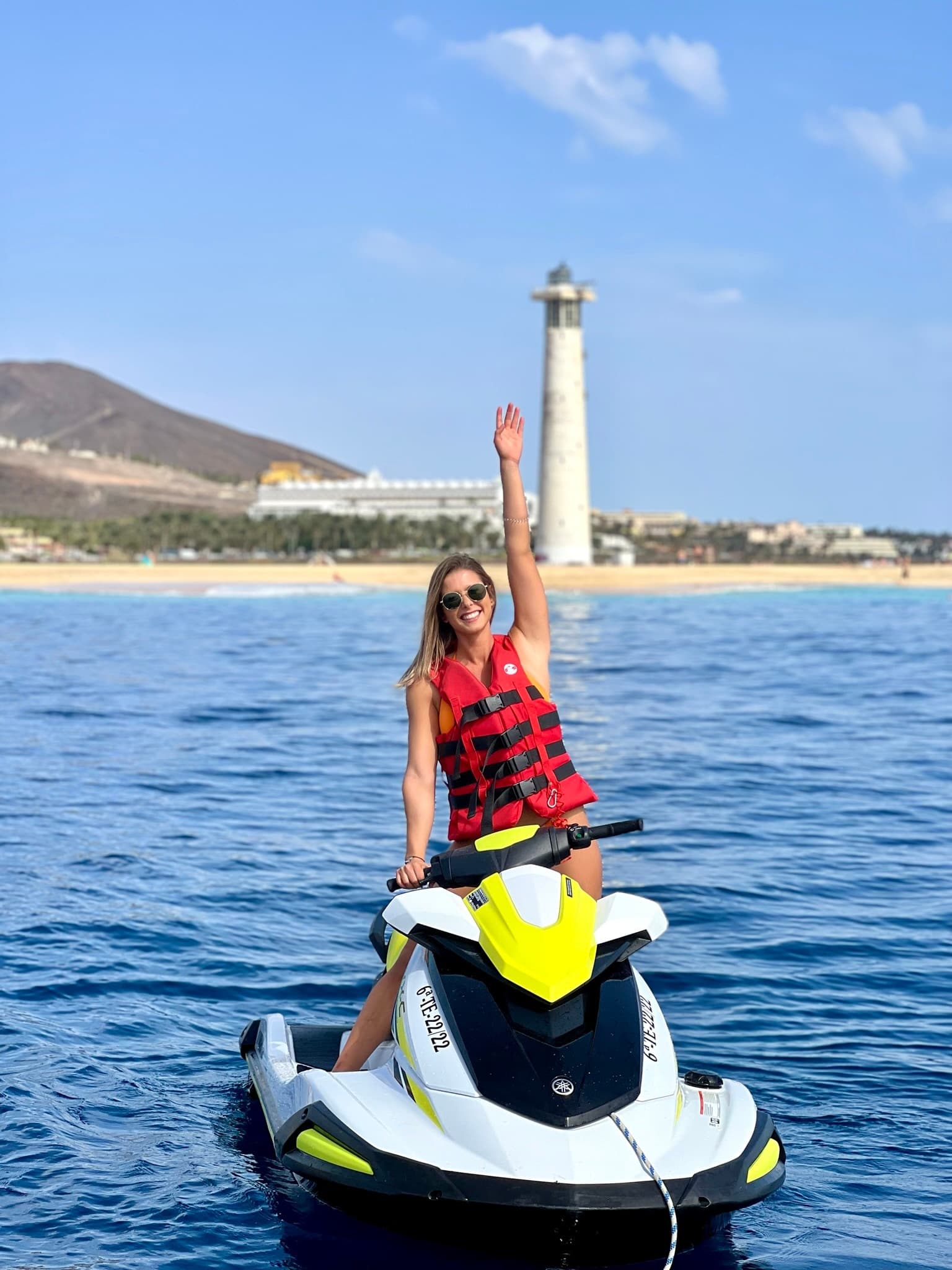 Woman on yellow jet ski near lighthouse in coastal Fuerteventura waters