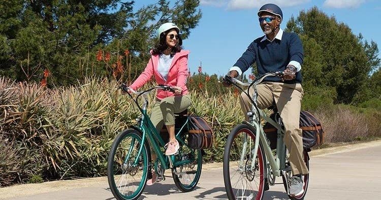Couple riding electric bikes on sunny coastal trail in park
