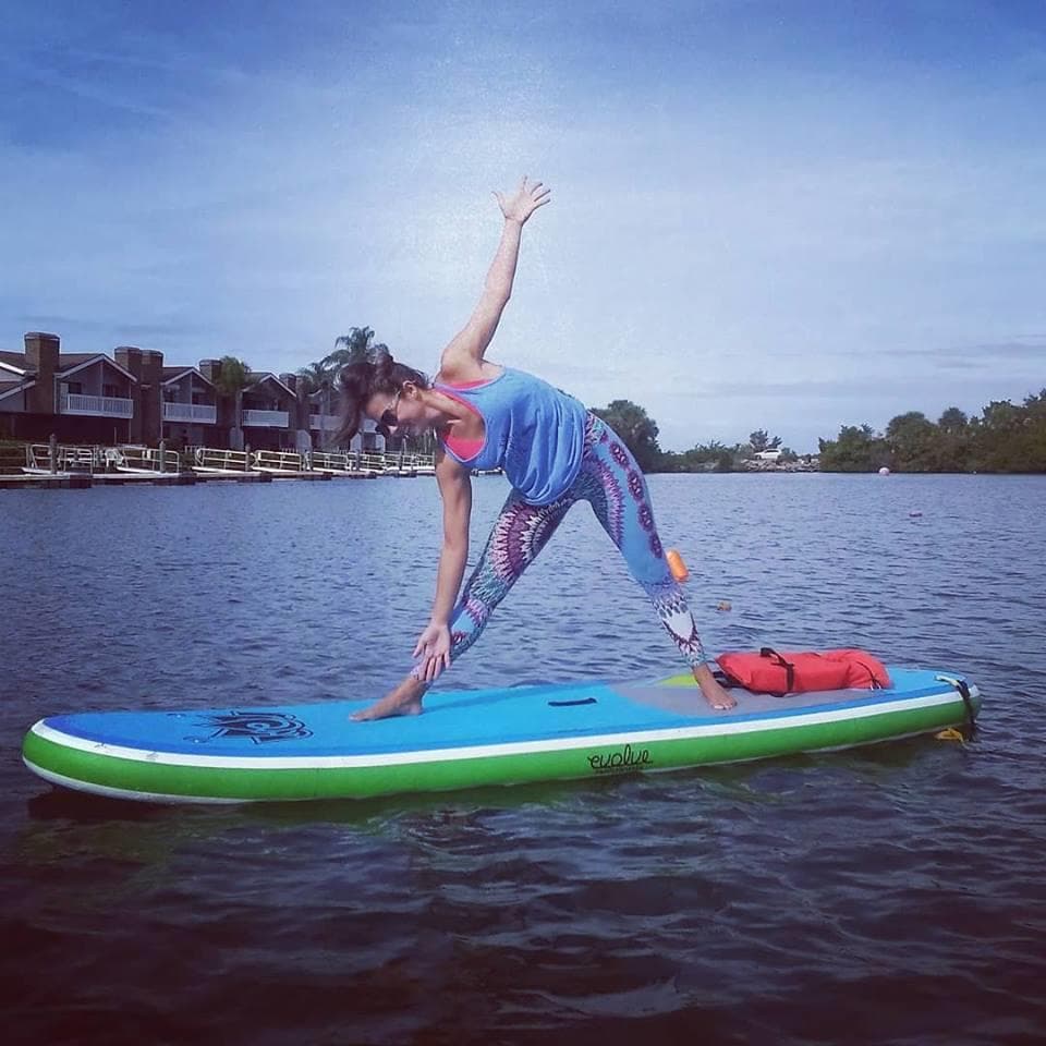 SUP yoga triangle pose on calm river with waterfront homes