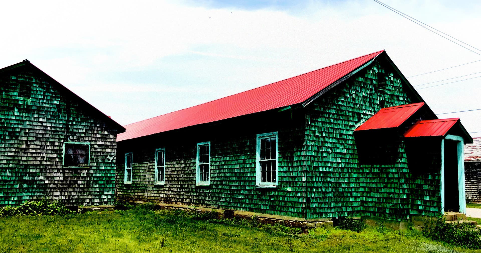 Green shingle camp building with red roof on grassy lawn