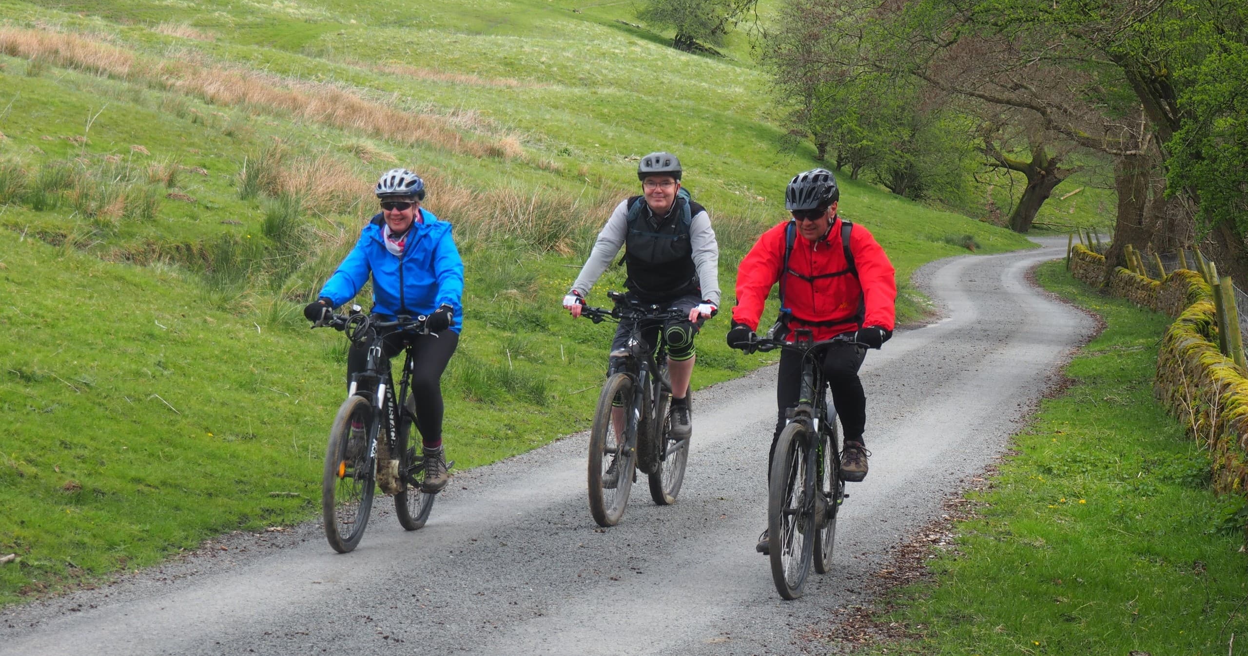 Three cyclists riding on country lane through green rolling hills