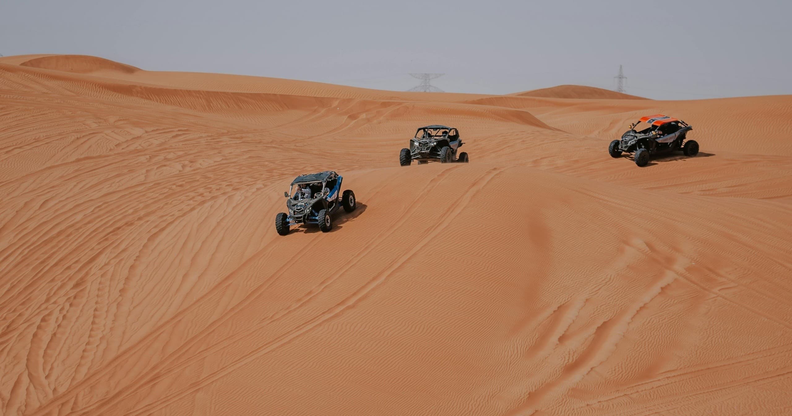 Three UTVs traversing orange desert dunes, off-road excursion