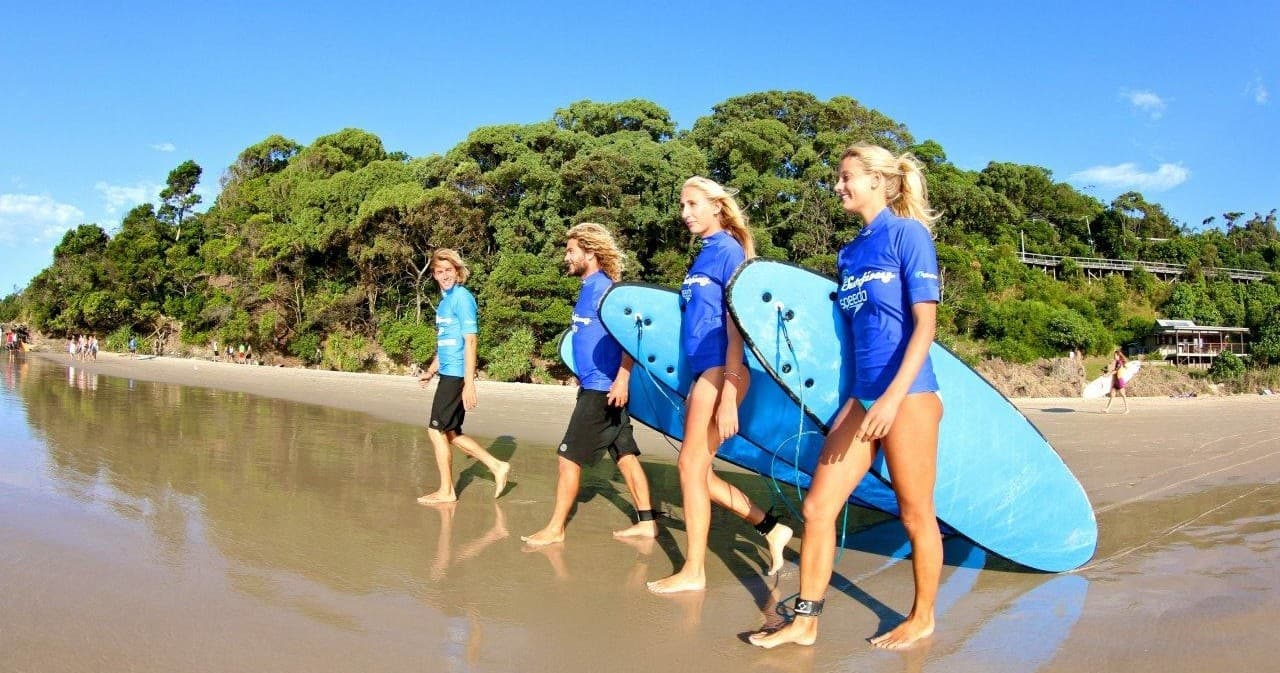 Group of surf students carrying blue boards on Byron Bay beach