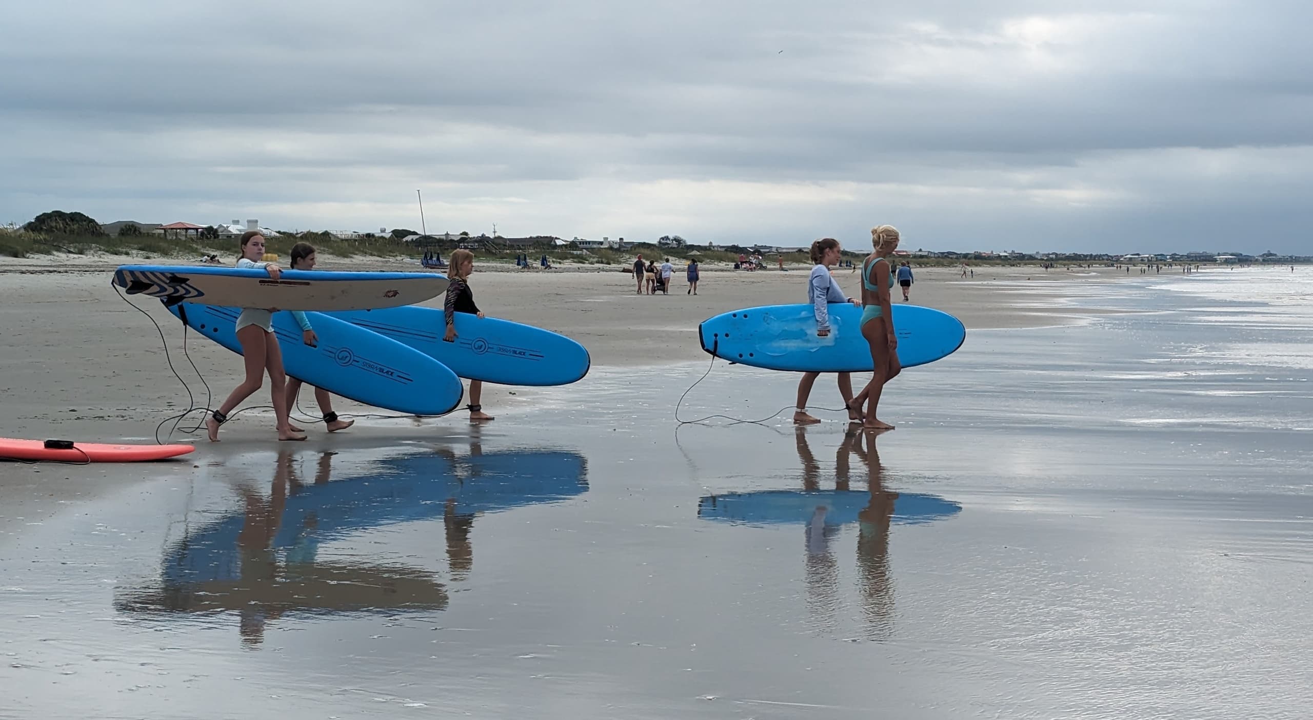 Surfers carrying blue boards on reflective wet sandy beach