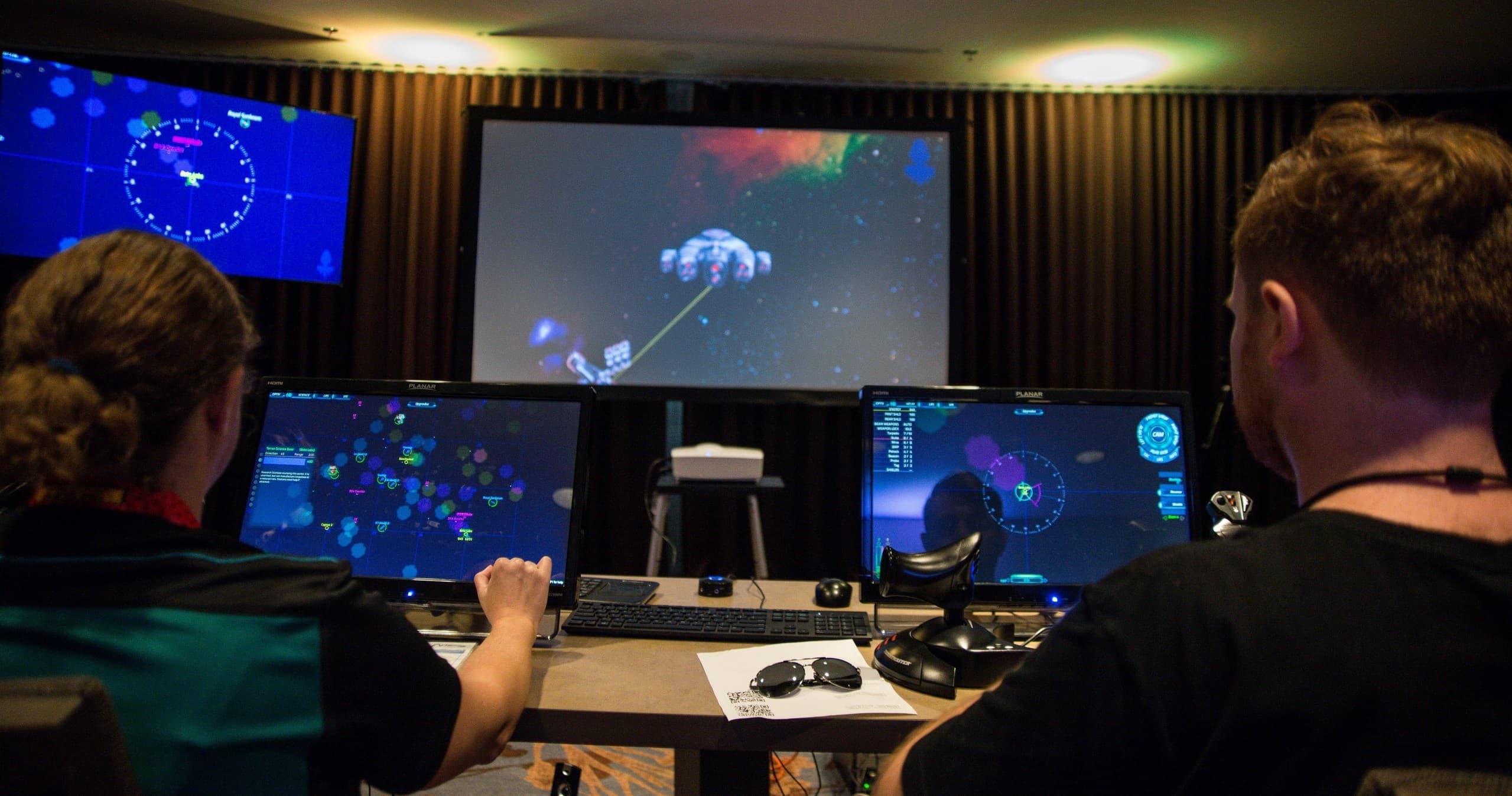 Players at desks using multi-monitor setup in indoor gaming event