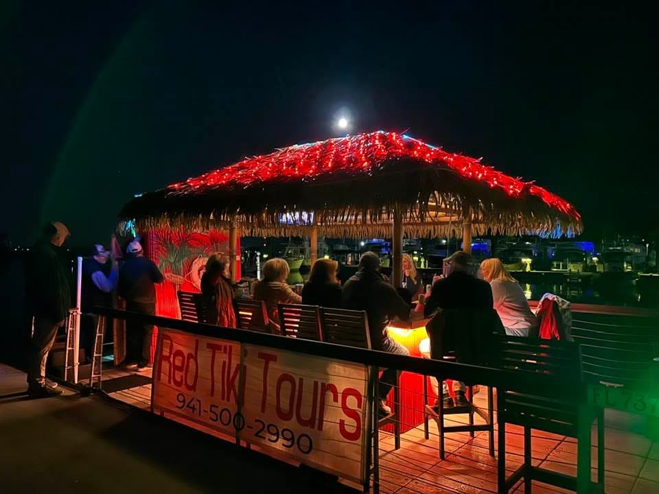 Nighttime tiki deck bar with patrons enjoying waterfront boat tour