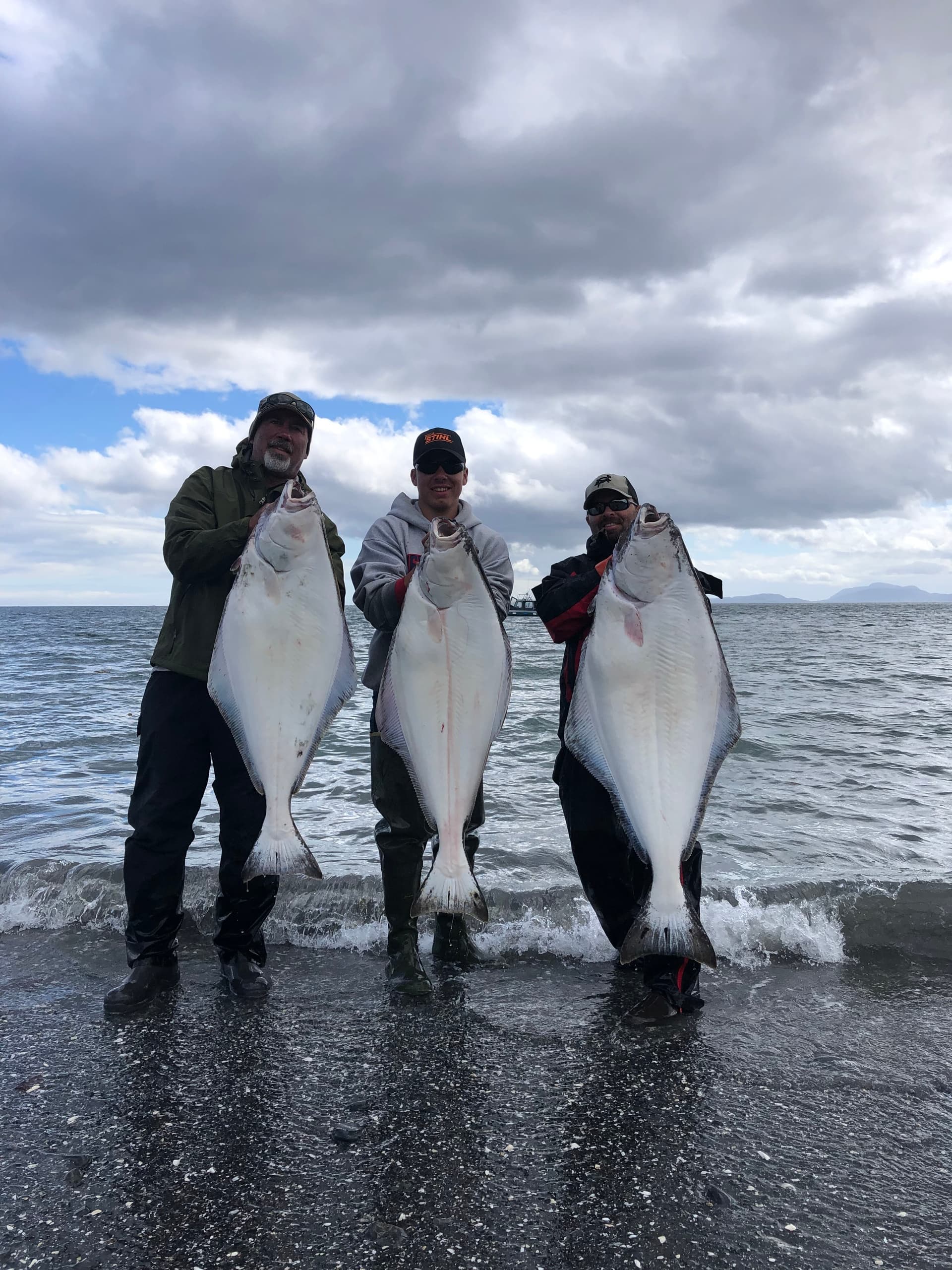 Three anglers displaying giant halibut on Alaska shoreline surf
