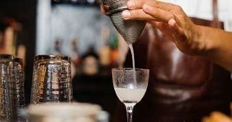 Bartender straining cocktail into coupe glass at Oxford bar counter