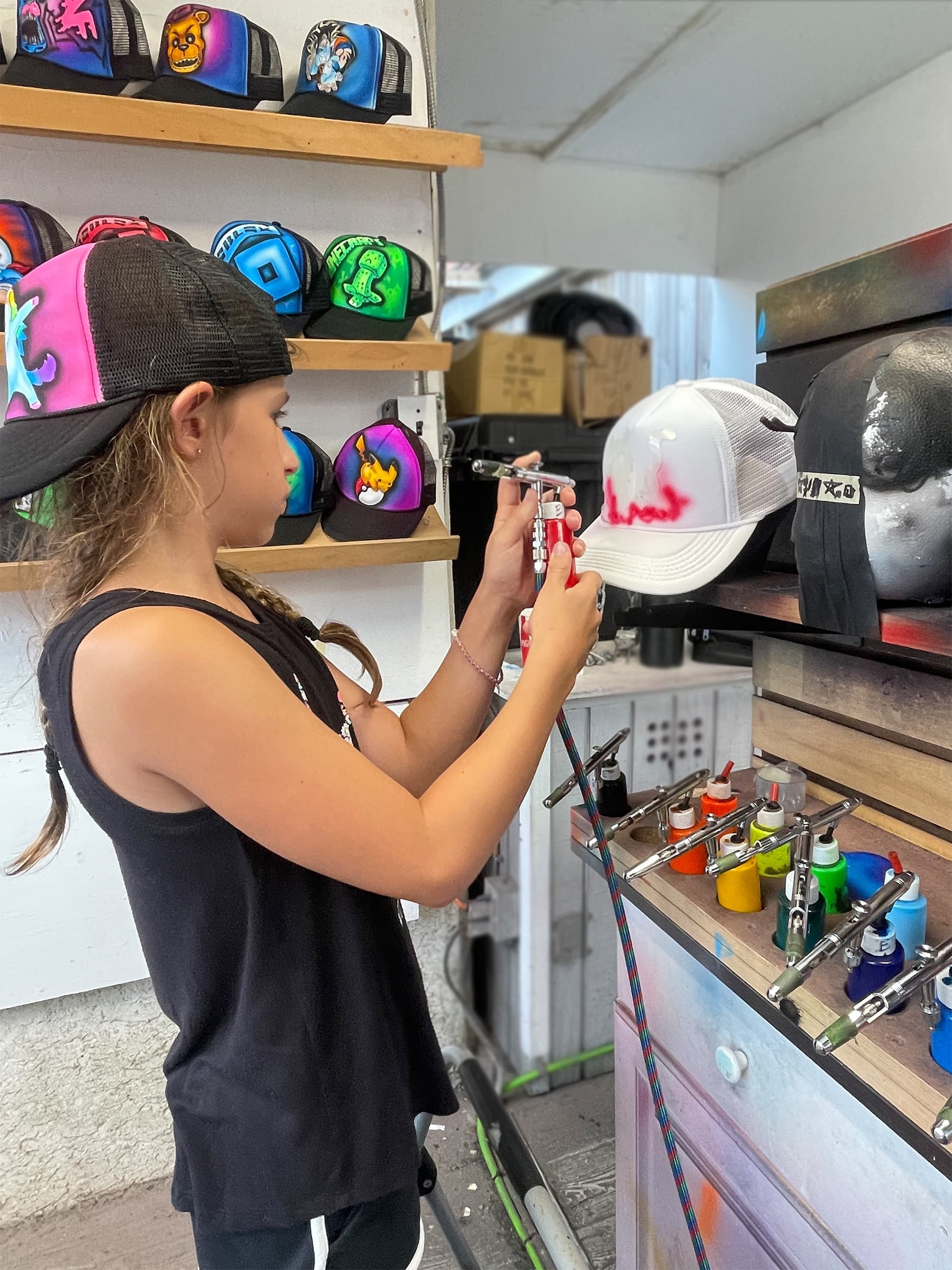 Girl airbrushing custom caps at indoor surfandspray shop counter