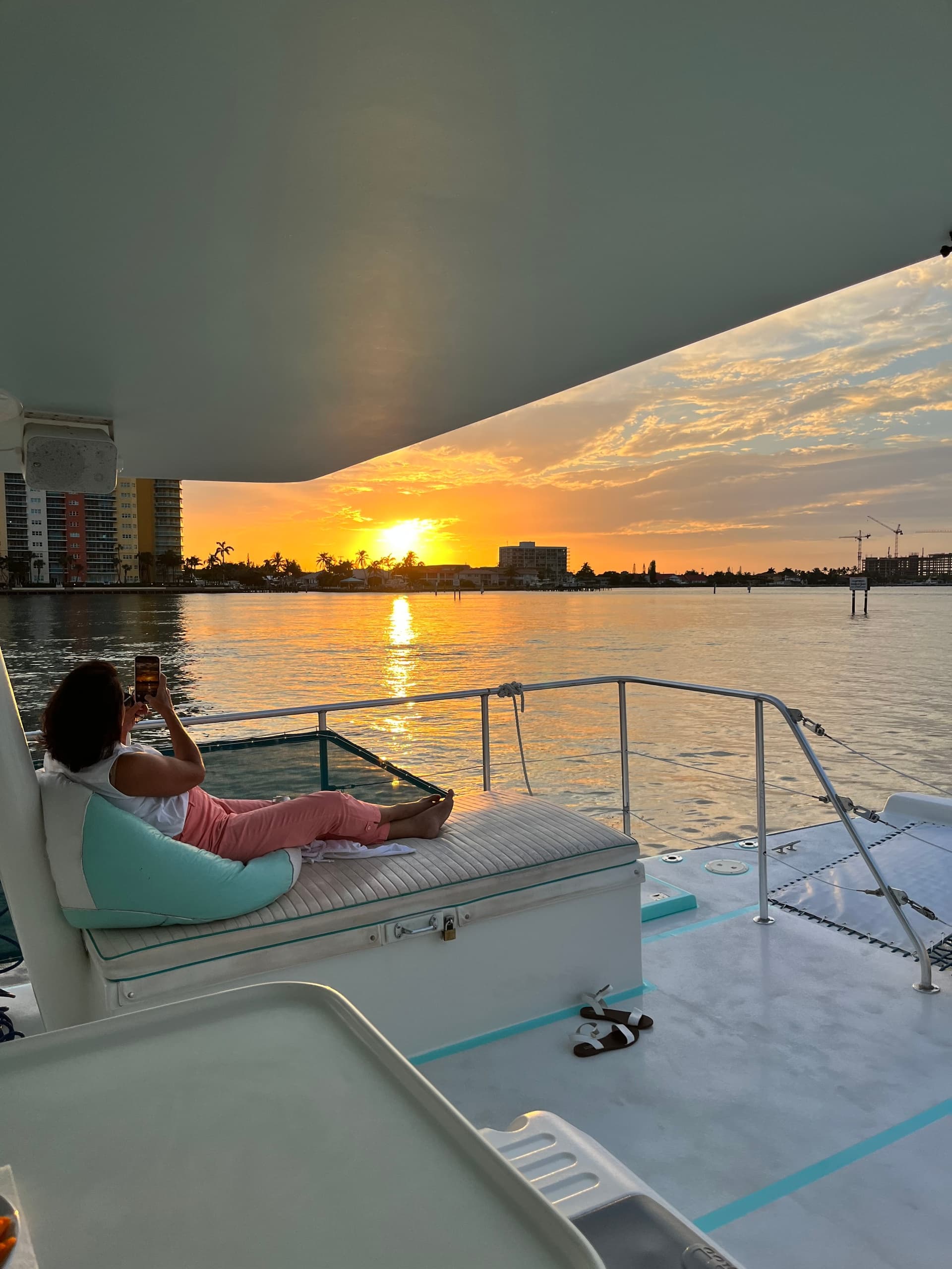 Sunset viewed from boat deck over calm harbor, coastal skyline
