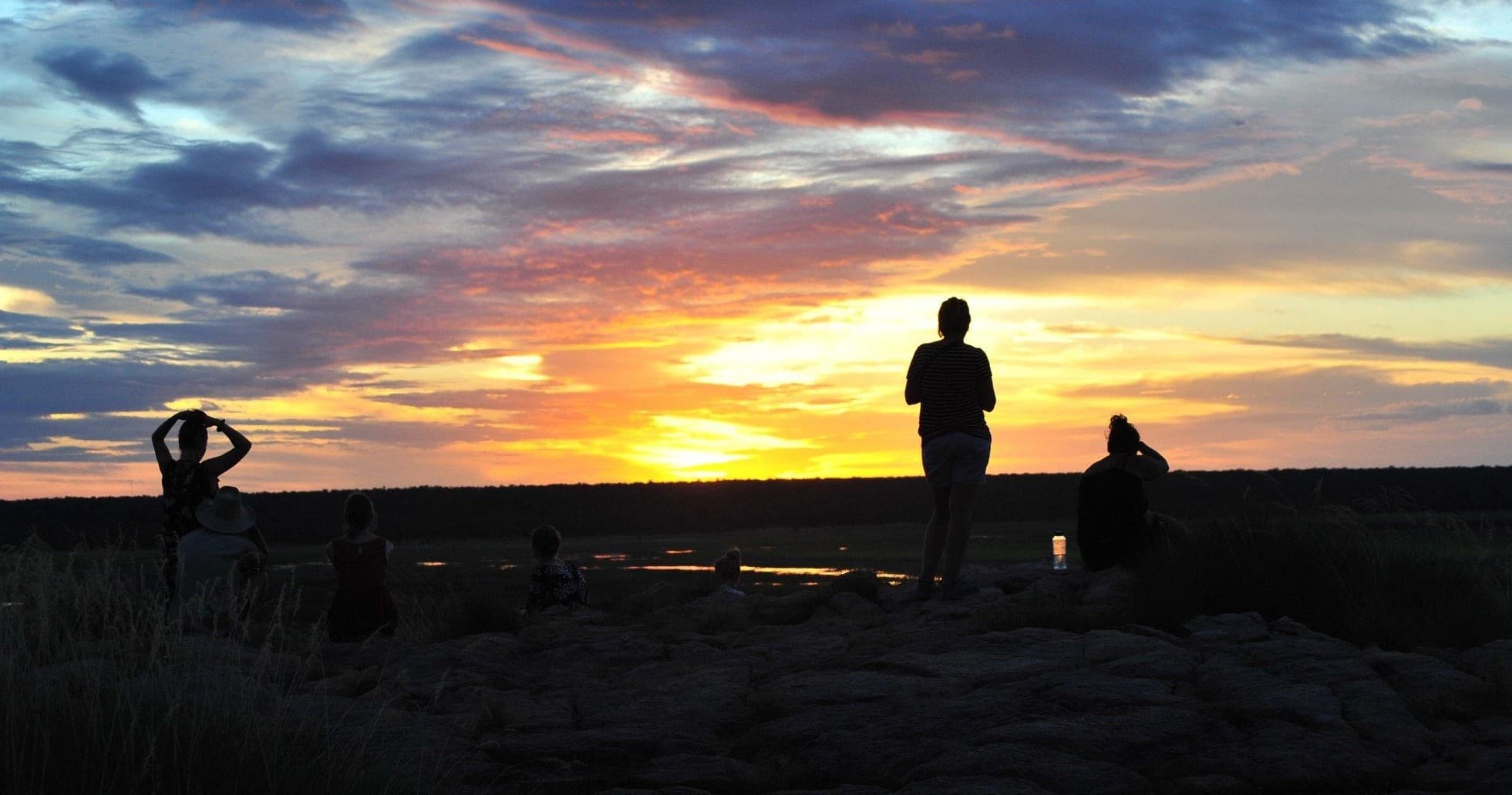 Silhouetted hikers watching coastal sunset, panoramic view