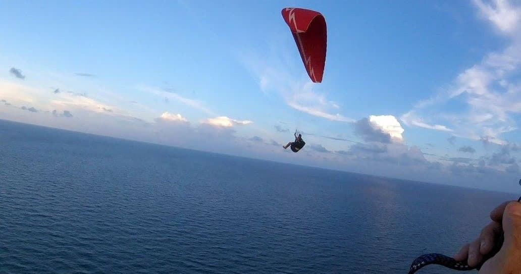 Tandem paraglider flying over open ocean with horizon view