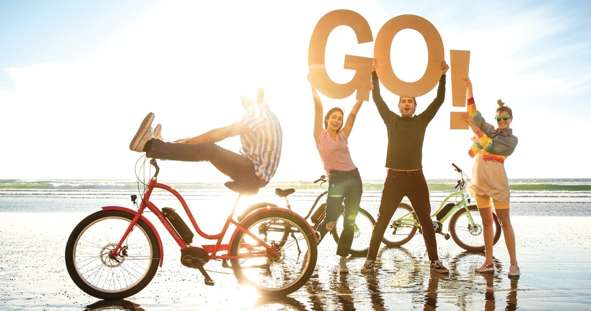 Friends cycling together on sunny beach shoreline at sunset