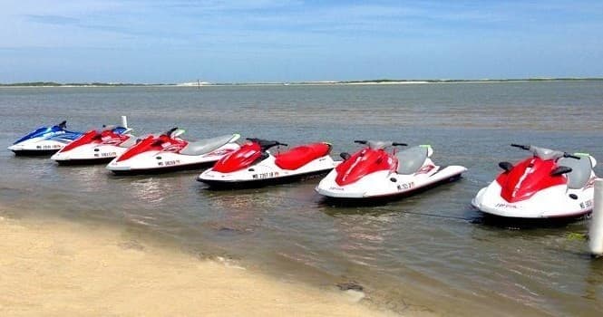 Row of parked jet skis on sandy beach under blue sky