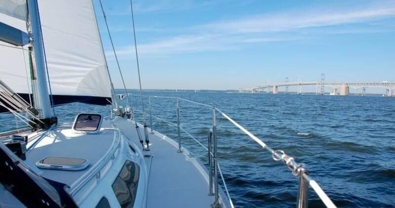 Sailboat deck cruising across open bay toward distant bridge