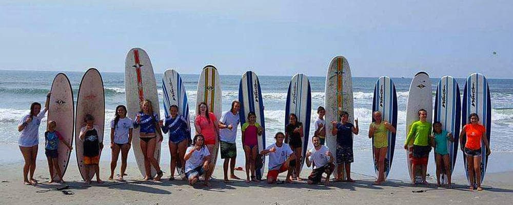 Group of surfers posing with boards on wide sandy beach