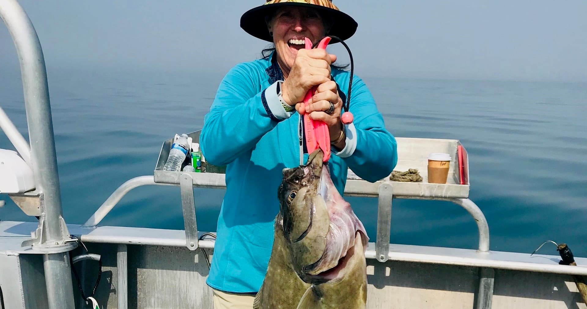 Angler holding large halibut on boat in calm coastal waters