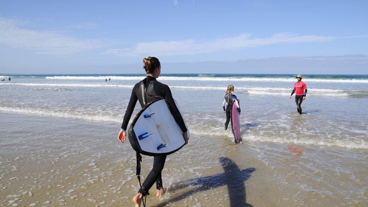Surfer carrying board walking into ocean at sandy beach