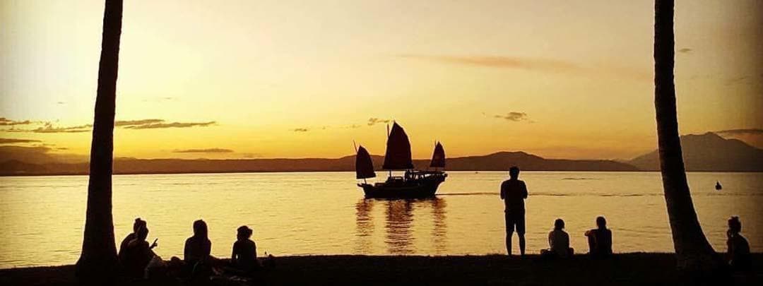 Junk boat sailing at sunset past tropical beach silhouettes