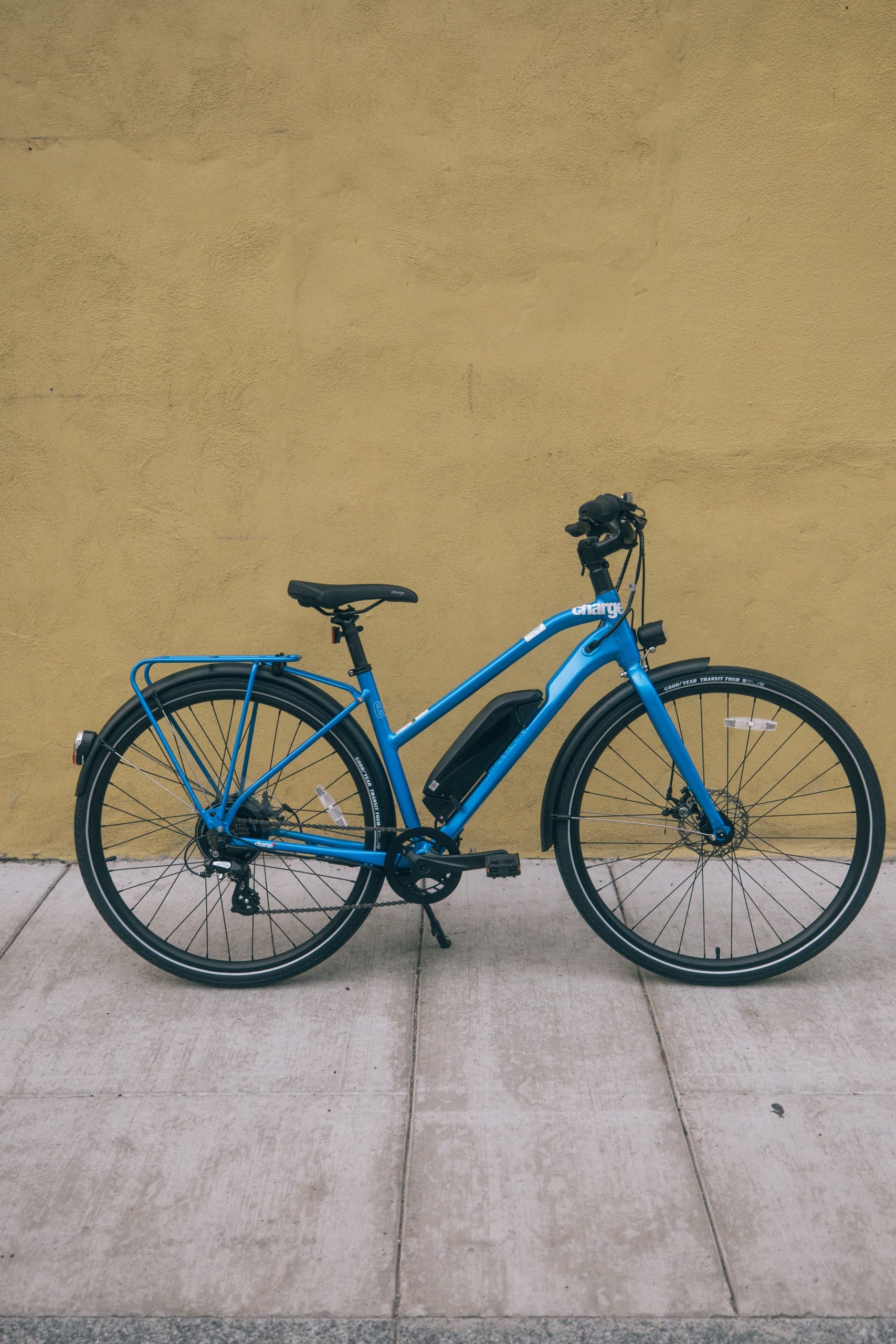 Blue fatbike parked against textured wall on paved sidewalk