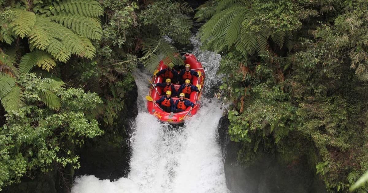 Inflatable raft plunging over narrow river waterfall in forest