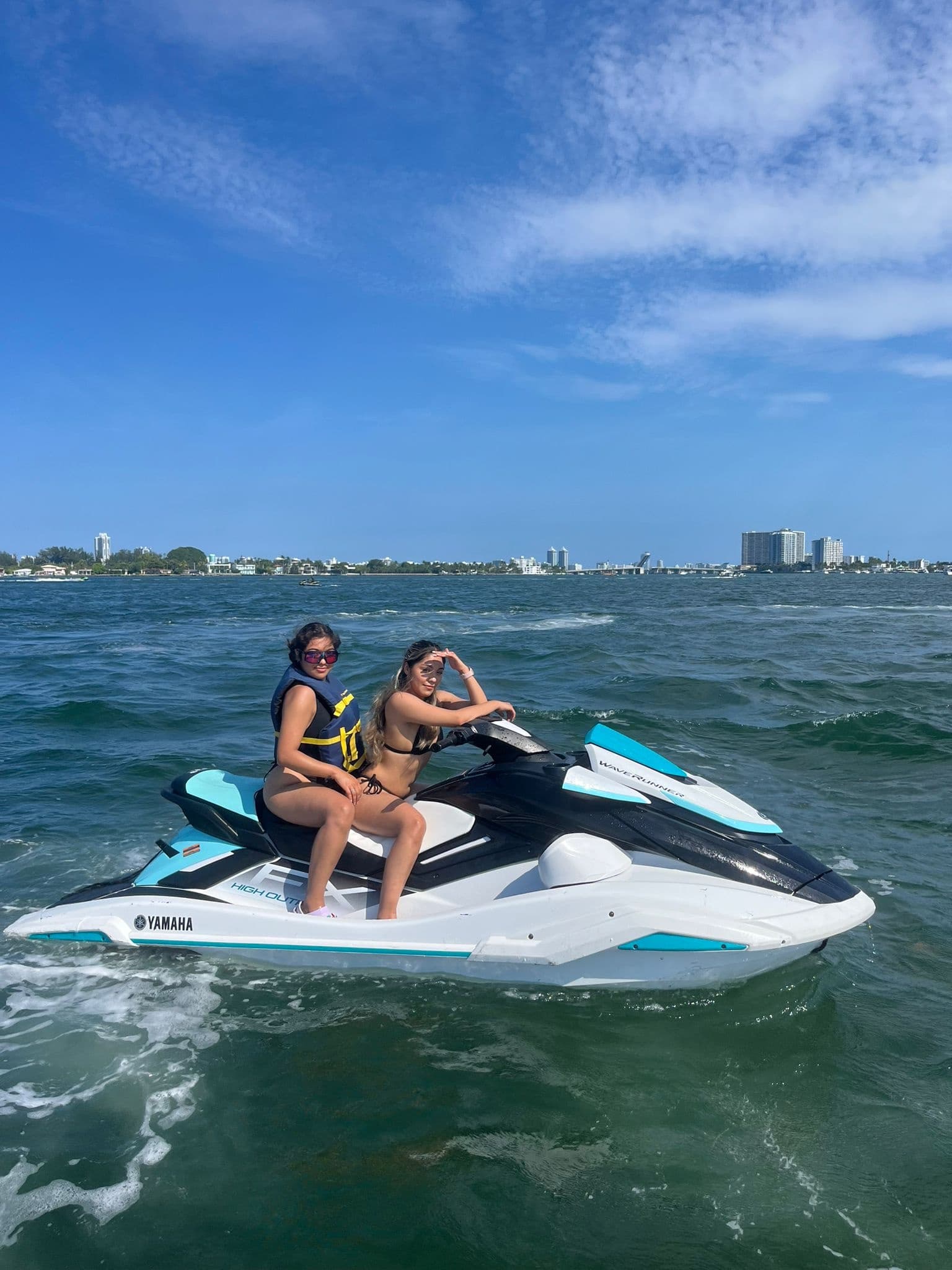 Two riders on a jet ski in coastal waters near city skyline enjoying ocean ride